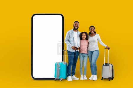 Photo for Happy family with luggage beside a large smartphone display conveying the idea of digital travel application technology, isolated on a yellow backdrop - Royalty Free Image