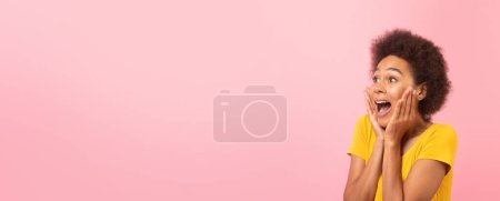 Foto de Una mujer afroamericana alegre en una parte superior amarilla está visiblemente emocionada o asombrada, con las manos en la cara, mirando a su izquierda con un fondo rosa - Imagen libre de derechos