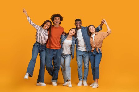 Téléchargez les photos : Une équipe multiethnique enchantée célèbre avec étreintes, dépeignant le zeste de l'amitié multiethnique sur un fond orange isolé - en image libre de droit