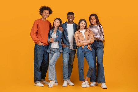 Téléchargez les photos : Un groupe joyeux et diversifié de cinq amis souriant et posant pour une photo avec un fond orange chaud - en image libre de droit
