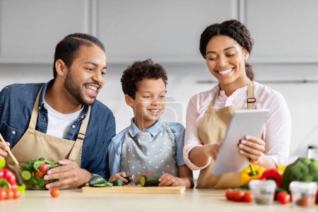 Photo for African American family shares a tablet while cooking in a kitchen, focusing on healthy food recipes - Royalty Free Image