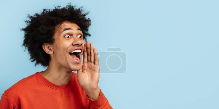 Foto de Hombre negro enérgico gritando o cantando, mano a boca, vistiendo un suéter naranja vibrante, sobre un fondo azul aislado. Transmite un mensaje o una liberación emocional, copia el espacio - Imagen libre de derechos