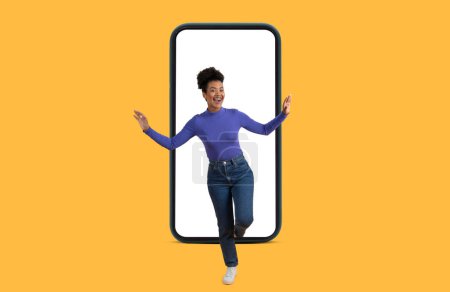 Téléchargez les photos : A woman is standing in front of a cell phone with white blank screen. She appears focused and engaged with the device, yellow background - en image libre de droit