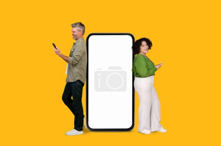 Man and woman of diverse ages using smartphones next to large phone mockup copy space on a yellow background