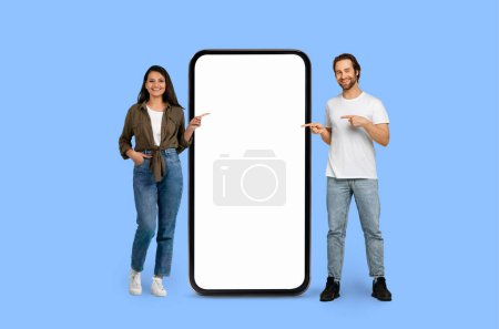 Ein lächelnder Mann und eine lächelnde Frau gestikulieren in Richtung einer leeren Smartphone-Display-Attrappe Kopierraum, nettes Angebot