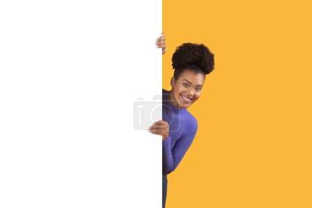 Eine Frau, die lächelt, während sie sich hinter Whiteboards für Werbung versteckt, glücklich und selbstbewusst wirkt. Sie blickt direkt in die Kamera, mit einem strahlenden Gesichtsausdruck.