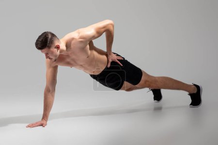 Foto de Un hombre se está equilibrando en un brazo mientras realiza un empuje hacia arriba, comprometiendo su núcleo, pecho y tríceps en un ejercicio desafiante para la fuerza y la estabilidad. - Imagen libre de derechos