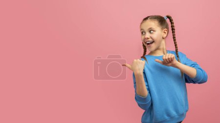Photo for Cheerful young girl with braided hair smiling and pointing at copy space with thumbs against a pink background - Royalty Free Image