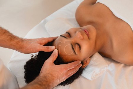 Close-up image captures a tranquil moment as african American lady enjoys temple massage in a spa setting