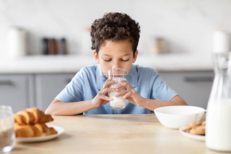 Photo for African American boy is captured drinking a glass of milk, portraying delight and the wholesomeness of breakfast time in a family kitchen setting - Royalty Free Image