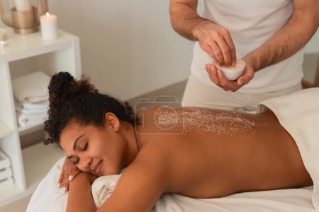Dans cette scène invitante, une dame noire est traitée à un gommage de dos luxueux dans un spa, affichant un sentiment de tranquillité et de soins