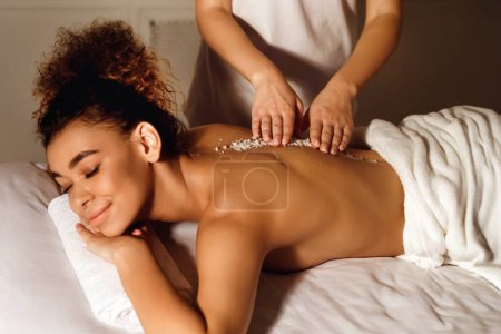 An African American woman is depicted receiving a back scrub treatment, emphasizing the themes of luxury spa care and relaxation for people