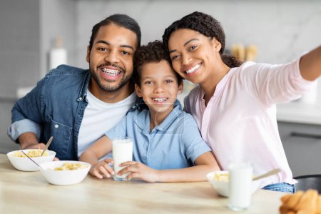 Photo for Cheerful African American family capturing a selfie while enjoying breakfast in a modern kitchen setting - Royalty Free Image