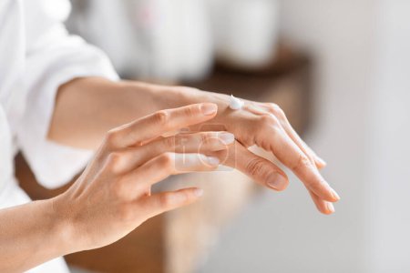 Téléchargez les photos : Une femme est vue appliquer une lotion de soin sur sa main, mettant en évidence les rituels quotidiens de salle de bain et de soins de la peau des dames millénaires, recadrées - en image libre de droit