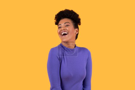 Mujer jovial hispana de pie frente a un fondo amarillo vibrante, expresando la risa. El lenguaje corporal de la dama transmite felicidad y alegría mientras se ríe de todo corazón.