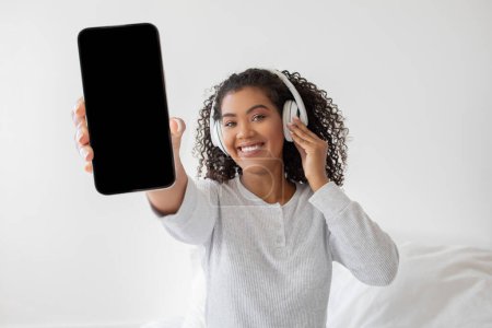 Photo for A woman wearing headphones is holding up a cell phone, possibly taking a selfie or talking on a video call. She looks engaged with the device, focusing on the screen. - Royalty Free Image