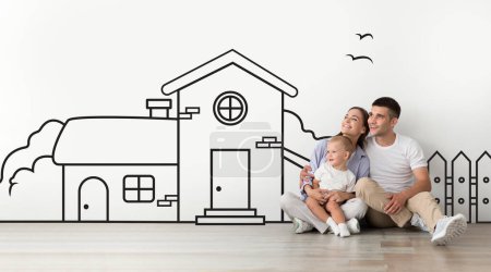 Photo for Young family father mother sitting with a child son against a wall with a drawn house. Mortgage concept - Royalty Free Image