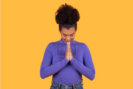 Photo for Hispanic woman standing with her hands folded in front of her face, exhibiting a gesture of thoughtfulness or contemplation. She appears deep in thought, with a focused expression on her face. - Royalty Free Image
