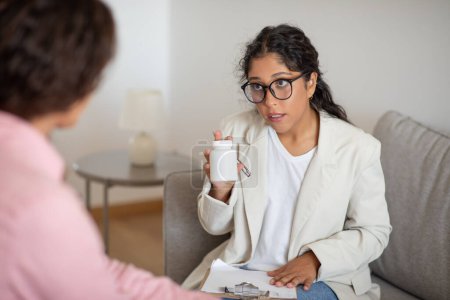 Photo for A focused woman healthcare provider explains medication details to a patient during a home visit consultation - Royalty Free Image