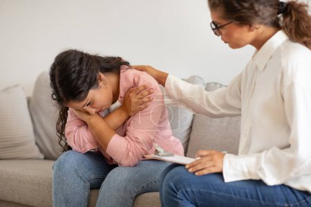 Young lady psychotherapist comforting crying woman client. Anxious lady have therapy session with counselor at modern clinic