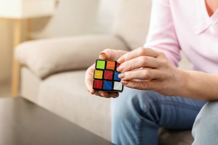 Photo for Cropped of woman is seen holding Rubik cube in her hands, trying to solve colorful puzzle. Her fingers twist and turn the cube, as she concentrates on aligning the colors to complete the challenge. - Royalty Free Image