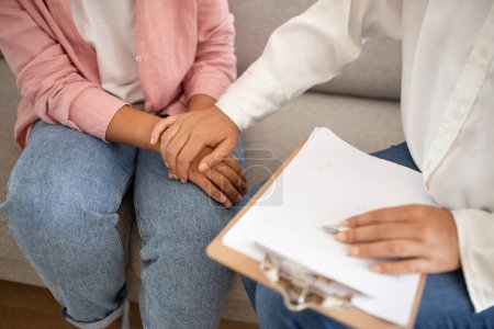 A counselor is holding a clients hand, offering comfort during a therapy session. The close-up captures the supportive touch and the clipboard in the counselors other hand, cropped