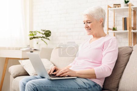 reife Frau tippt auf ihrem Laptop, sitzt zu Hause, freier Raum