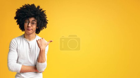 Foto de ¿Viste eso? Hombre africano escéptico señalando a un lado en el espacio vacío sobre fondo panorama naranja - Imagen libre de derechos