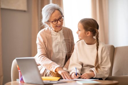 Una mujer mayor y una joven están sentadas juntas en una mesa, ambas mirando atentamente la pantalla de un portátil. Parecen participar en una discusión o actividad en el ordenador