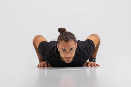 A man is positioned face down on the ground, with his hands shoulder-width apart and pushing his body up and down in a rhythmic motion
