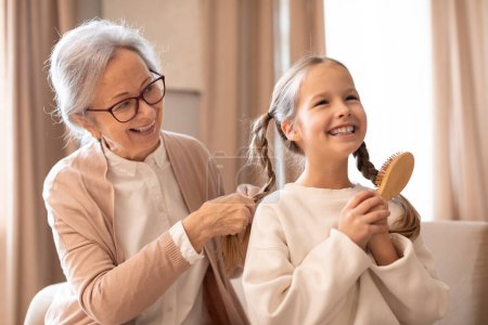 Photo for An older woman is gently combing a young girls hair, sitting closely together in a simple and heartfelt moment of care and bonding. - Royalty Free Image