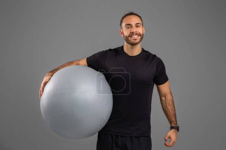 A man standing holding a big ball with his right hand. The mans grip is strong and steady, showing his strength and control over the object