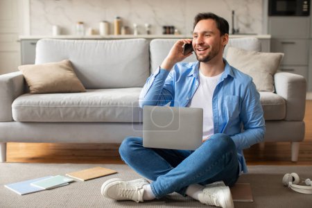 Ein Mann sitzt auf dem Boden, multitasking mit einem Laptop und telefoniert mit einem Handy. Er wirkt fokussiert und engagiert in seiner Arbeit und balanciert die Technologie effizient aus.