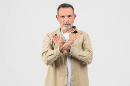 Ein älterer Mann steht aufrecht, die Hände vor der Brust gefaltet, in einer selbstbewussten und aufmerksamen Haltung und zeigt Stoppgeste auf weiß