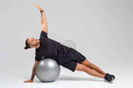 A man is performing various exercises on an exercise ball, engaging his core muscles and improving balance and stability, on grey background