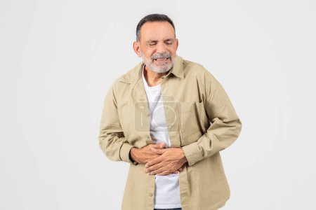 Photo for A senior man is shown with his hands placed on his stomach, indicating discomfort or pain. He appears to be experiencing abdominal issues, possibly due to indigestion or illness. - Royalty Free Image