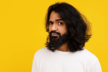 Ein perplexer junger indischer Mann mit gerunzelter Braue steht vor einem leuchtend gelben Hintergrund und zeigt einen verdutzten Gesichtsausdruck, Großaufnahme