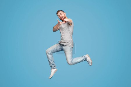 Gotcha. Emotionale Millennial rothaarige Kerl zeigt mit dem Finger auf Kamera, volle Länge, blauer Studiohintergrund, Kopierraum