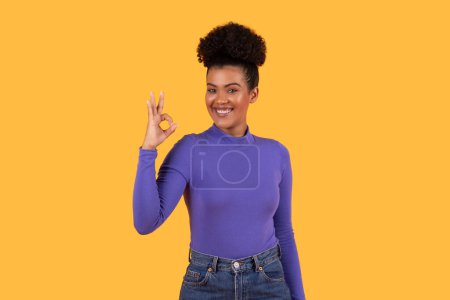 Photo for Hispanic woman wearing a purple shirt is standing and making okay gesture with her hand, isolated on yellow background - Royalty Free Image