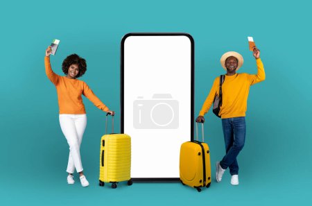 Foto de Pareja afroamericana juguetona en amarillo se encuentra junto a una pantalla de teléfono inteligente de gran tamaño, que ilustra la integración de los viajes con la tecnología digital - Imagen libre de derechos