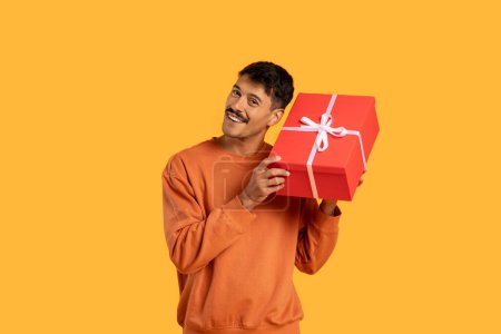 Téléchargez les photos : Un homme tient une boîte-cadeau rouge avec un ruban blanc dans les mains. Il semble se préparer à offrir le cadeau à quelqu'un de spécial, faisant preuve de prévenance et de générosité.. - en image libre de droit
