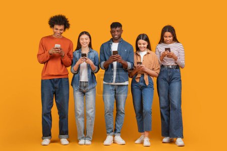 Eine internationale Gruppe junger Freunde, in ihre Smartphones vertieft, verkörpert multiethnische, multirassische Konnektivität im digitalen Zeitalter, isoliert auf orange
