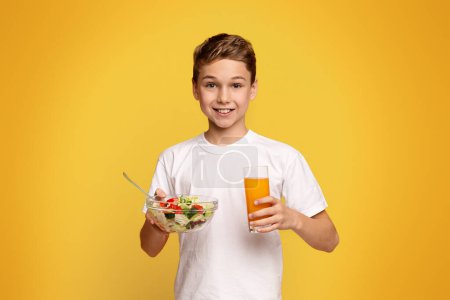 Foto de Sonriente niño comiendo ensalada de verduras y jugo de naranja fresco, fondo estudio de naranja - Imagen libre de derechos