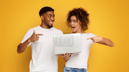 Photo for Cheerful millennial black man and woman pointing at laptop, like website, orange background - Royalty Free Image