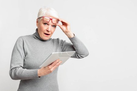 Photo for A senior European woman looks surprised while using a digital tablet, embodying curiosity and the evolving experience with s3niorlife - Royalty Free Image
