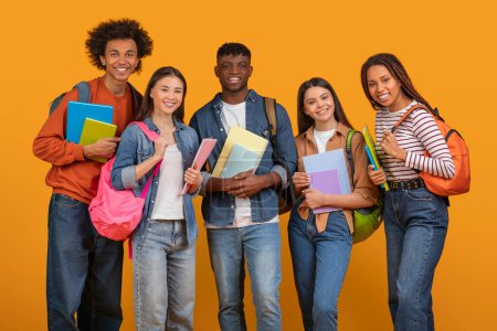Foto de Un alegre equipo internacional de estudiantes amigos con coloridos libros y mochilas, que representan la educación multiétnica y multirracial aislada en naranja - Imagen libre de derechos