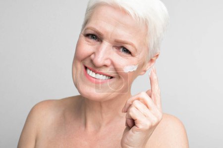 Foto de Una alegre anciana europea aplicando crema facial, reflejando la esencia de s3niorlife y espíritu juvenil - Imagen libre de derechos