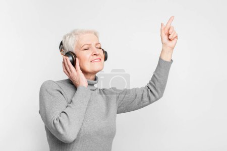 Photo for An elderly European woman in a turtleneck smiles while listening to music with headphones, representing joyful s3niorlife - Royalty Free Image