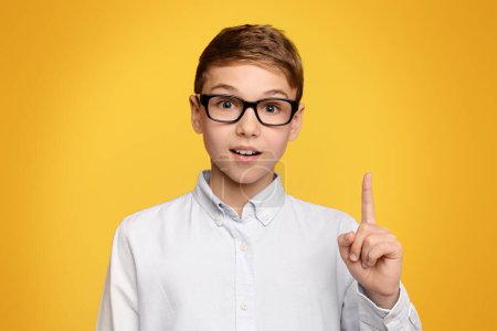 Foto de Pequeño genio. inteligente adolescente en gafas teniendo idea, apuntando su dedo hacia arriba, naranja fondo del estudio - Imagen libre de derechos