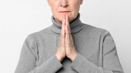 This European elderly woman holds her hands in a prayer position, reflecting a moment of gratitude or reflection, highlighting key aspects of s3niorlife
